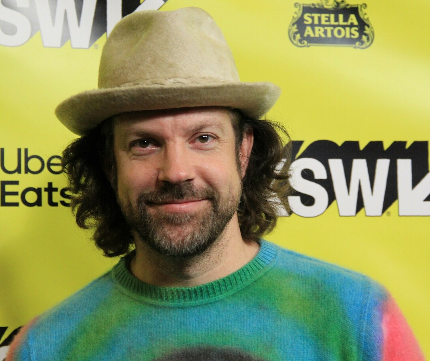 Jason Sudeikis, chapeau clair et cheveux longs, lors d’un festival, sans la moustache de Ted Lasso